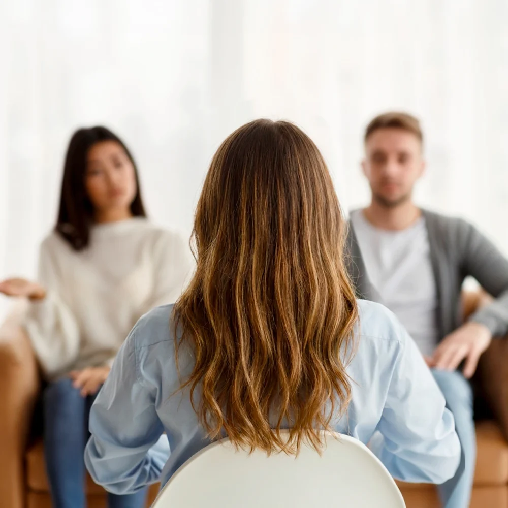 Couple en séance de thérapie avec une thérapeute, vus de dos